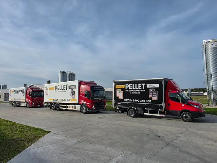 Dwie czerwone ciężarówki Volvo i Iveco Daily z zabudową PELLET na placu przy silosach